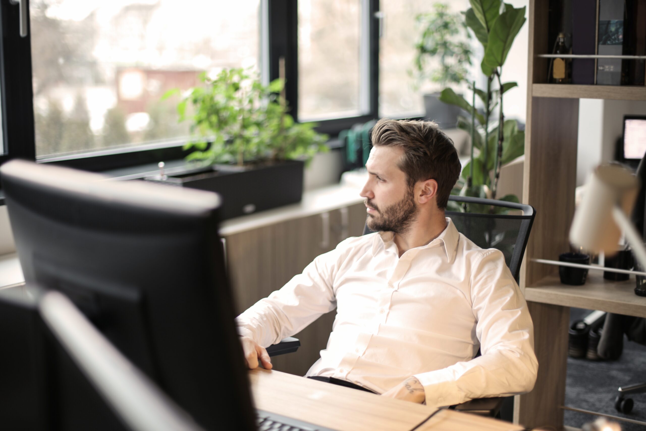 man in white business shirt sitting at a desk and looking out the window