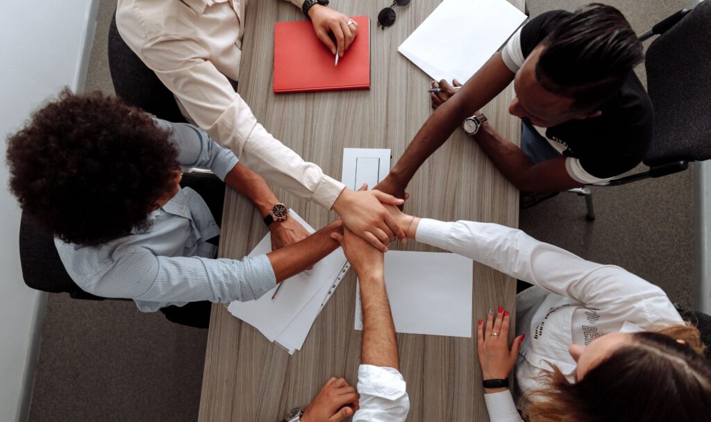 Overhead view of a diverse team placing hands together in a sign of unity during a meeting.